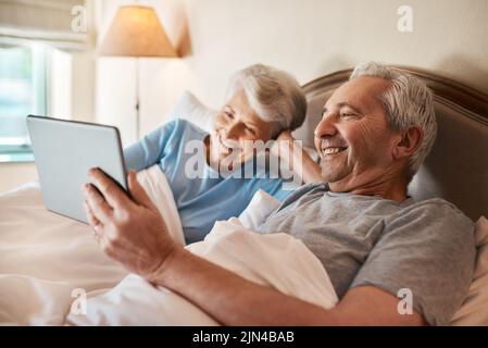 Sembra un buon film da guardare. Una coppia anziana felice seduta insieme a letto e utilizzando un tablet in una casa di cura. Foto Stock
