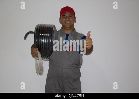 Elettricista sorridente con i pollici che trasportano un rotolo di tubo corugato e sonda per un impianto elettrico. Fai da te lavori di casa Foto Stock