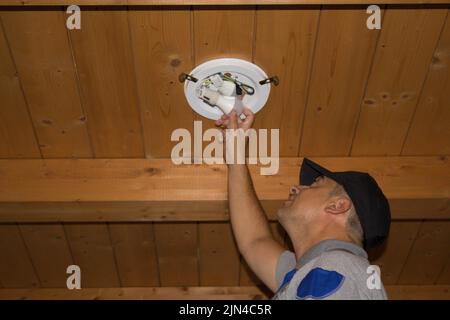 Immagine di un elettricista su una scala che sostituisce una lampadina. Faccia esso voi stessi lavoro Foto Stock