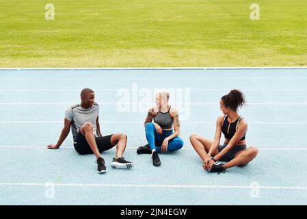 Rilassarsi dopo la gara. Scatto completo di un gruppo di atleti che si siedono insieme dopo una sessione di allenamento di squadra su una pista da corsa. Foto Stock