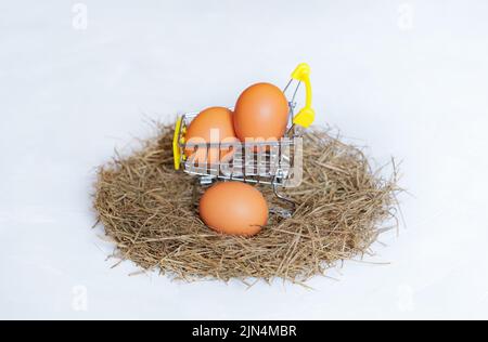 Carrello in miniatura con uova di pollo posto in un nido di fieno isolato su sfondo neutro. Concetto da azienda agricola a tavola. Foto Stock