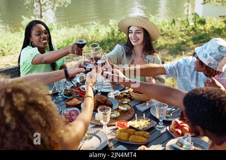 Gruppo di giovani ad alta angolazione che tostano con bicchieri di vino durante la cena all'aperto in estate Foto Stock