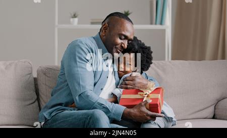 Little amorevole figlia carina si congratula con papà il compleanno dà dono uomo adulto chiude gli occhi in previsione di sorpresa sorpreso amatissimo gode espresso Foto Stock