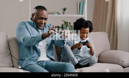 Felice afroamericano padre e figlia hanno divertimento insieme padre giocare video gioco su console con bambino ragazza uso controller sedersi sul divano Foto Stock