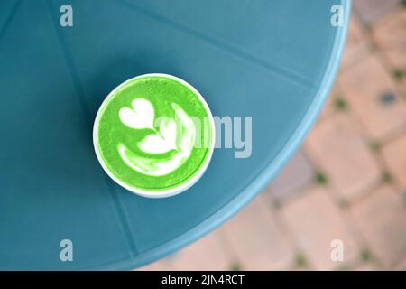 La vista dall'alto della tazza d'arte color verde matcha e' sul tavolo di plastica nel cafe'. Stile a disposizione piatta. Foto Stock