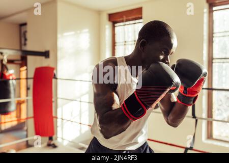 Giovane pugile maschile in posizione di combattimento indossando guanti da boxe. Giovane sportivo che ha una sessione di allenamento di boxe in palestra. Foto Stock