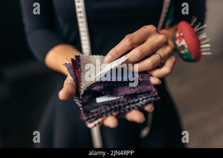 Primo piano delle mani femminili che tengono i campioni di tessuto. Concentratevi sulle mani femminili selezionando un nuovo tessuto da campioni diversi. Foto Stock