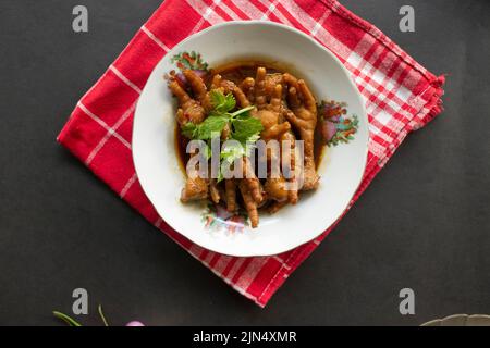 Piedi di pollo piccanti con sedano, peperoncino, cipolla, aglio servito con un piatto bianco sul tavolo Foto Stock