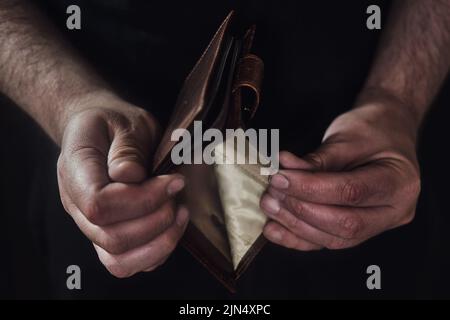 Portafoglio vuoto senza soldi nelle mani di un uomo su uno sfondo nero Foto Stock
