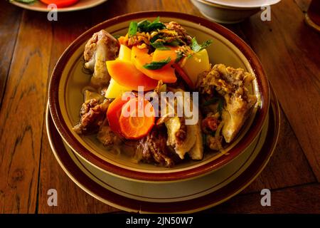 Deliziosa zuppa di costolette o IgA di zuppa in una ciotola servita con carote di patate e sedano su sfondo di legno Foto Stock