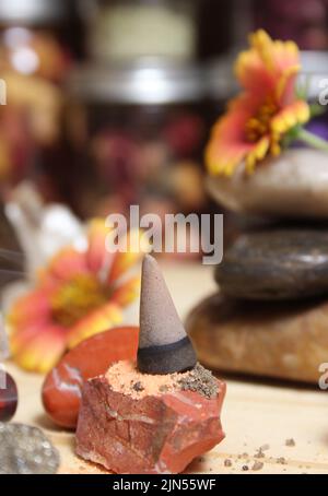 Cono di incenso su lastra di pietra con cristalli di Chakra e fiori Foto Stock