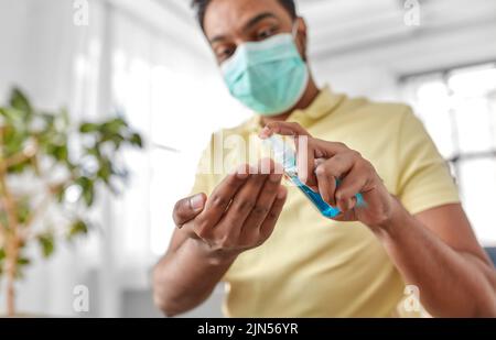 primo piano di uomo in maschera applicazione igienizzatore per le mani Foto Stock