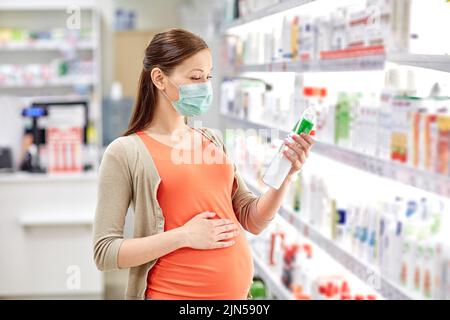 donna incinta in maschera scelta lozione in farmacia Foto Stock