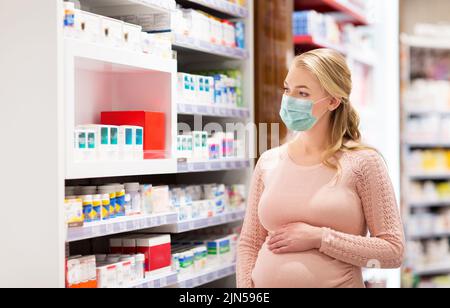 donna incinta in maschera con medicinali in farmacia Foto Stock