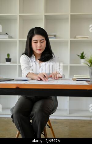 Donna d'affari asiatica o analista finanziario femminile, focalizzata e professionale, che lavora sul foglio di calcolo del rapporto finanziario presso la sua scrivania d'ufficio. Foto Stock