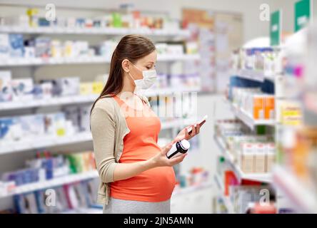 donna incinta in maschera con medicinale in farmacia Foto Stock