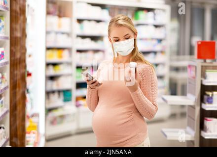 donna incinta in maschera con medicinale in farmacia Foto Stock