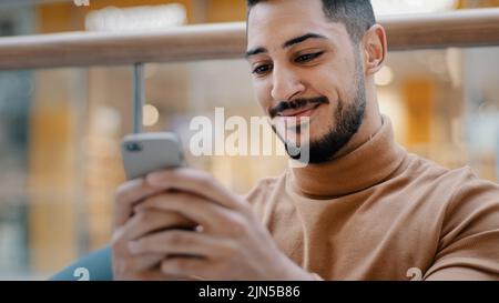 Primo piano giovane arabo ragazzo tenendo telefono guardando lo schermo smartphone sorridente ricevere bel messaggio e-mail navigazione web su dating sito controlla sociale Foto Stock