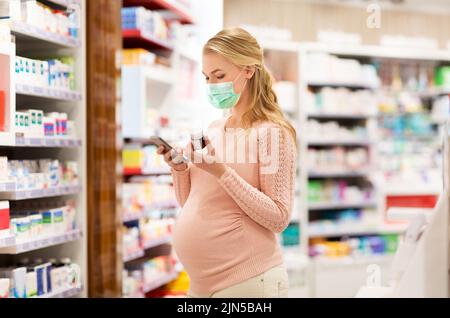 donna incinta in maschera con medicinale in farmacia Foto Stock