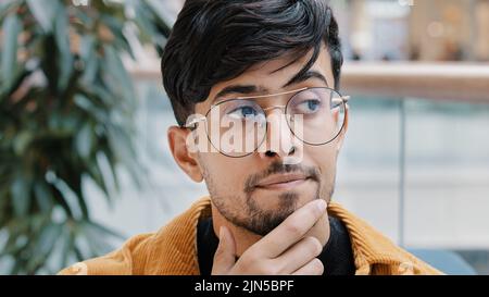 Headshot giovane e pensivo uomo indiano premuroso che tiene mano sul mento pensando in profondità nel pensiero nella ricerca decide la soluzione al problema difficile Foto Stock