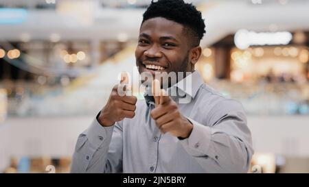 Primo piano felice giovane bell'uomo afroamericano che guarda la macchina fotografica sorridendo posa mostrando il gesto hey voi pistole che fanno segno di approvazione di scelta Foto Stock