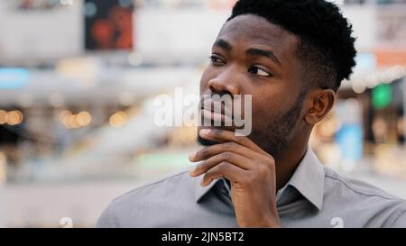 Primo piano enigled concentrato pensivo serio africano americano giovane uomo guardare via tiene la mano sul mento pensa risolve il problema arriva con nuovo Foto Stock