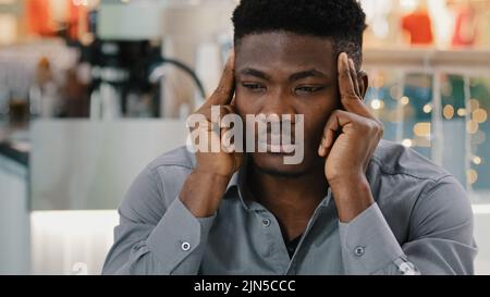 Primo piano triste malsano afroamericano uomo strofinare templi sente grave pressione di mal di testa che soffre di emicrania sintomo preoccupato ragazzo stressato Foto Stock