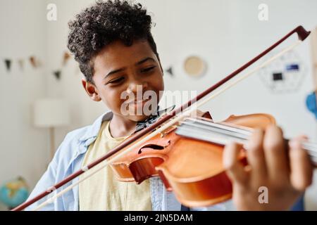 Sorridente ragazzo africano che suona il violino a casa durante la lezione Foto Stock