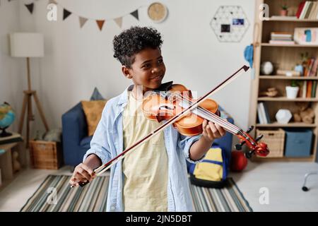 Ragazzo africano che suona il violino durante la lezione mentre si trova nella sua stanza a casa Foto Stock