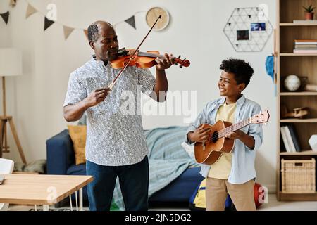 Ragazzino africano che suona la chitarra con il suo insegnante che suona il violino durante la lezione di casa Foto Stock