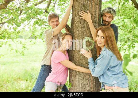 Il gruppo di amici sente il relax mentre abbraccia un albero su una passeggiata nella foresta Foto Stock