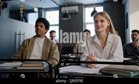 Gli studenti studiano in classe gruppo giovani persone felici seduti alla scrivania a lezione ascoltare la lezione imparare nuovo argomento comunicare discutere adolescenti Foto Stock
