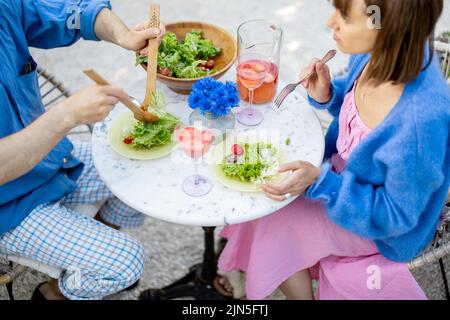 Il giovane uomo e la donna hanno un pranzo con insalata sana e bevande all'aperto Foto Stock