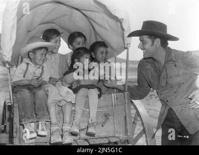 ERROL FLYNN sul set location candida con i bambini messicani durante le riprese di ROCKY MOUNTAIN 1950 regista WILLIAM KEIGHLEY storia Alan le May musica Max Steiner Warner Bros. Foto Stock