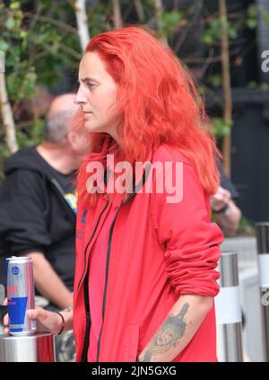 Blackpool, Lancashire, UK Agosto 6 2022 BA giovane woam con capelli rosso brillante che scorre e giacca corrispondente che tiene una bevanda in scatola durante il Blackpool Reb Foto Stock
