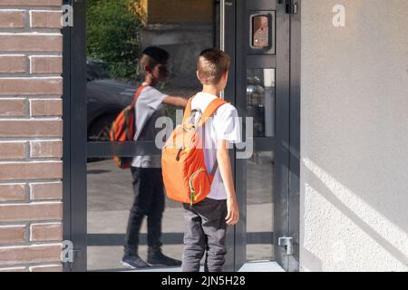 Carino ragazzo studente con uno zaino scuola apre la porta della casa. Un bambino che ritorna a casa dopo la scuola vicino alla porta della casa. Torna a scuola Foto Stock