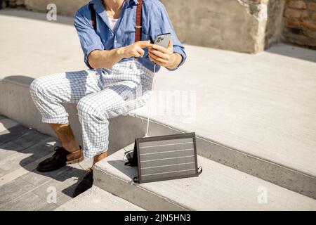Uomo carica il telefono dal pannello solare portatile Foto Stock