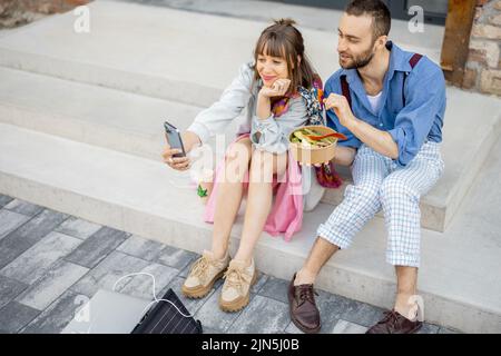 I colleghi mangiano cibo sano take away e parlano al telefono all'aperto Foto Stock