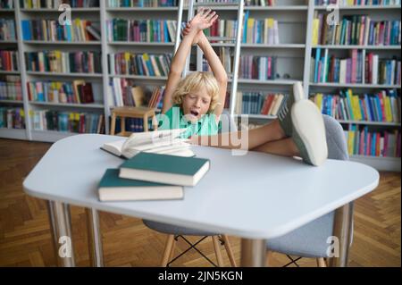 Scolaro che fa un esercizio di stretching nella sala lettura Foto Stock
