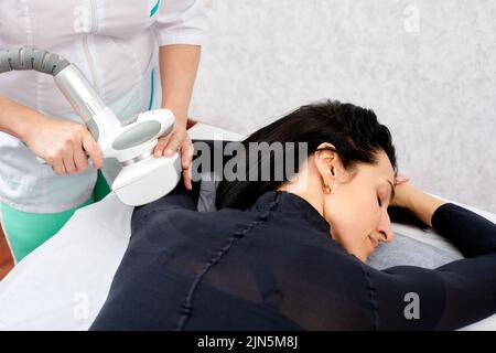 Donna in tuta nera per massaggio GPL acqua potabile prima del massaggio GPL. Concetto anticellulite per la cura del corpo. Macchina massaggio GPL sullo sfondo Foto Stock