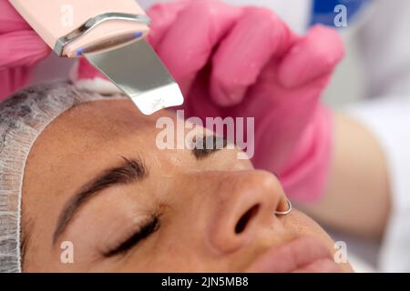 Medico di bellezza con scrabber ultrasonico che fa la procedura di pulizia ultrasonica del viso. Cosmetologia e cura della pelle del viso. Foto Stock