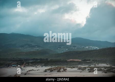 La spiaggia di sabbia di Guincho a Cascais, Portogallo, con le colline sullo sfondo sotto il cielo nuvoloso blu Foto Stock