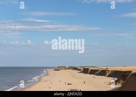 Persone sulla spiaggia di Happisburgh, Norfolk, con le scogliere (erodendo a causa dell'erosione costiera) sullo sfondo. Foto Stock
