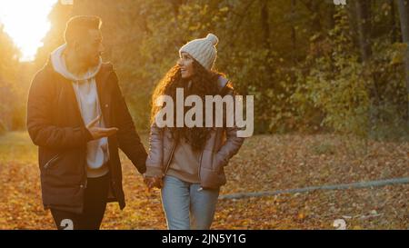 Felice giovane coppia in amore a piedi in autunno parco al tramonto romantico sera data in natura eccitato ragazzo gioioso comunica con la ragazza parlare Foto Stock