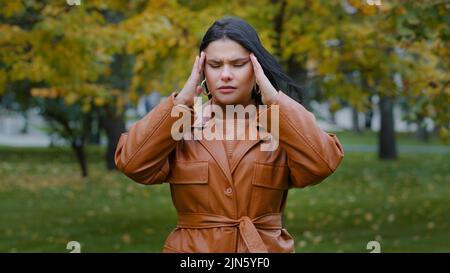 Closeup sconvolto ragazza ispanica in piedi all'aperto soffrono di mal di testa malessere dolore rubs tempio agitato giovane donna preoccupata di male Foto Stock