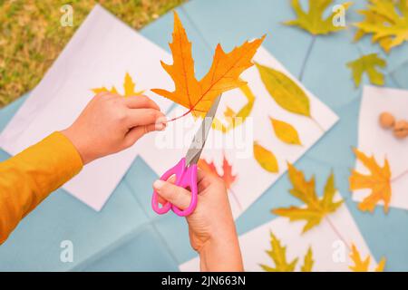 Fai da te arte bambini gioco creativo imparare fuori scuola parco di apprendimento all'aperto. Bambini laboratorio bambini forbici taglio foglie arte artigianato bambini fatto a mano autunno Foto Stock