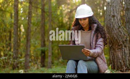 Attraente donna ingegnere forestale in casco protettivo inserisce i dati nel portatile prende azione di rimboschimento giovane esperto specialista femminile Foto Stock