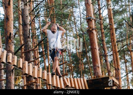 Un uomo supera un ostacolo in una città di corda. Un uomo in un parco di corda foresta Foto Stock