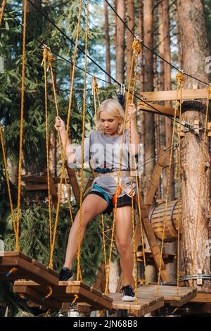 Una ragazza passa un ostacolo in una città di corda. Una ragazza in un parco di corda foresta Foto Stock