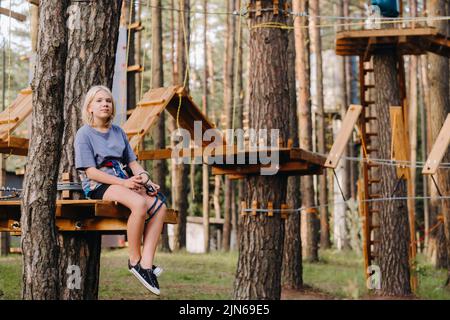 Una ragazza passa un ostacolo in una città di corda. Una ragazza in un parco di corda foresta Foto Stock